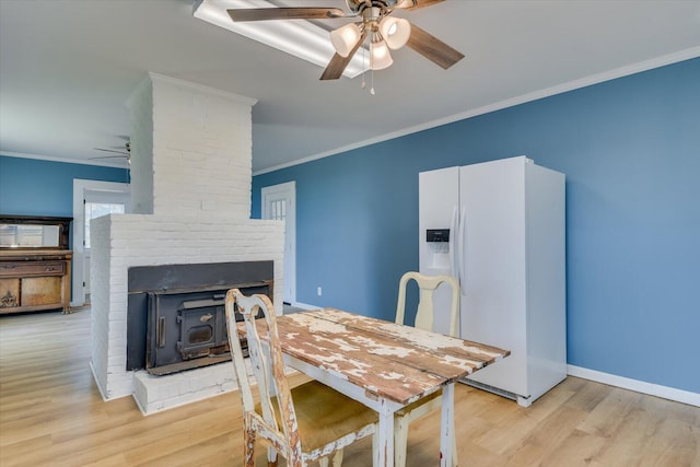 dining space with light hardwood / wood-style floors, a wood stove, ceiling fan, and crown molding