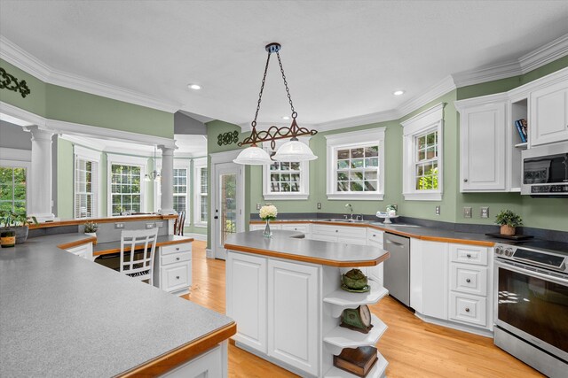 kitchen with appliances with stainless steel finishes, ornate columns, decorative light fixtures, white cabinets, and a center island