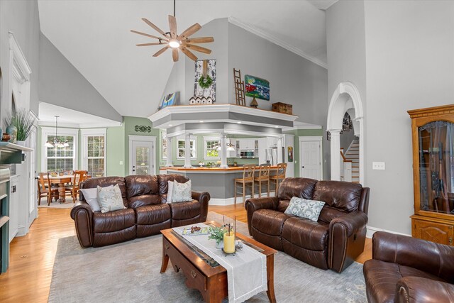 living room featuring a towering ceiling, ceiling fan with notable chandelier, decorative columns, and light hardwood / wood-style floors