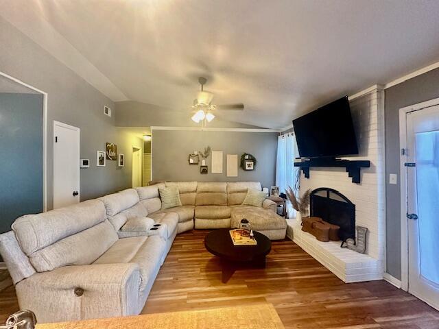 living room with hardwood / wood-style floors, vaulted ceiling, a brick fireplace, and ceiling fan