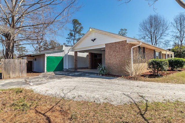 view of front of property with brick siding, an attached carport, fence, an outdoor structure, and driveway