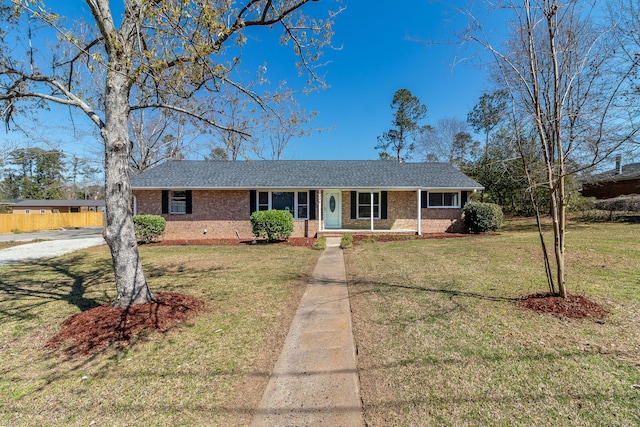 ranch-style house with brick siding, covered porch, a front yard, and roof with shingles