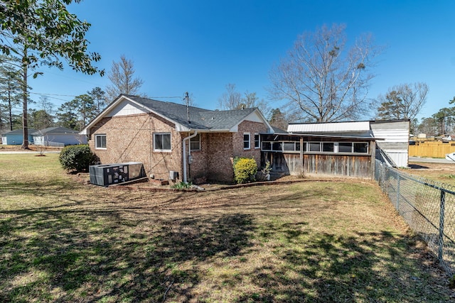 rear view of house with brick siding, central AC unit, a lawn, and fence