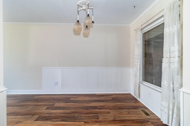 spare room with visible vents, a chandelier, a wainscoted wall, ornamental molding, and wood finished floors