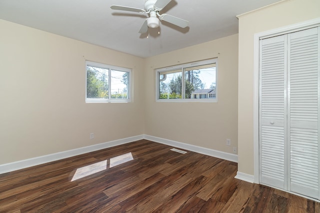 unfurnished bedroom with a closet, a ceiling fan, dark wood-type flooring, and baseboards