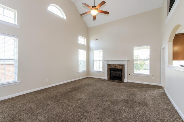 unfurnished living room with a tile fireplace, a high ceiling, dark carpet, and ceiling fan