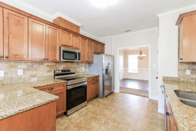 kitchen with light stone countertops, appliances with stainless steel finishes, ornamental molding, pendant lighting, and a chandelier