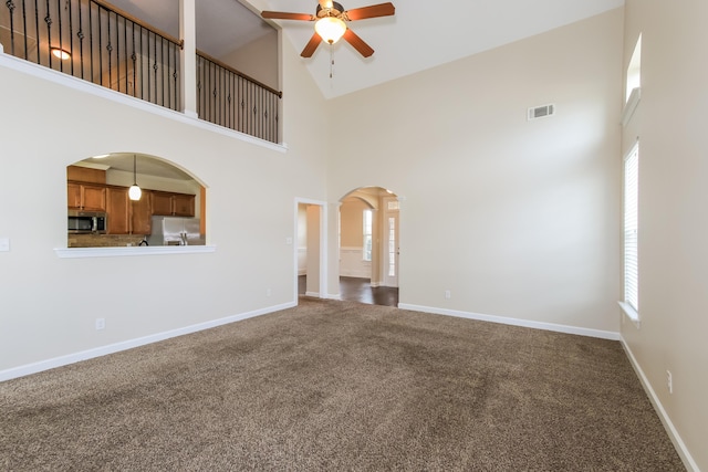 unfurnished living room featuring carpet flooring, high vaulted ceiling, ceiling fan, and ornate columns