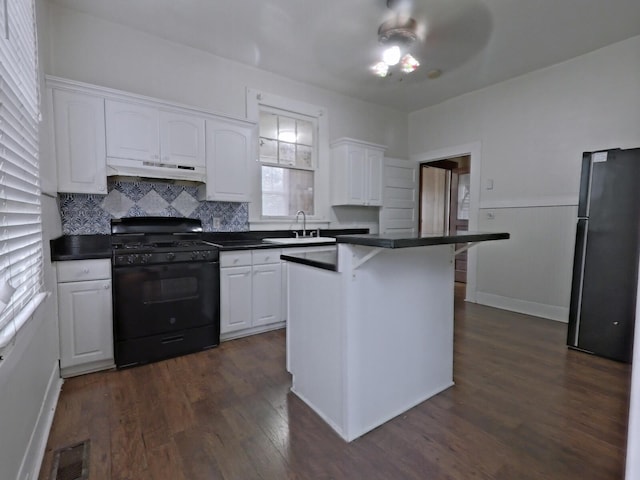 kitchen with black gas range oven, under cabinet range hood, freestanding refrigerator, white cabinetry, and a sink