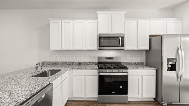 kitchen with light stone countertops, appliances with stainless steel finishes, dark hardwood / wood-style flooring, sink, and white cabinetry