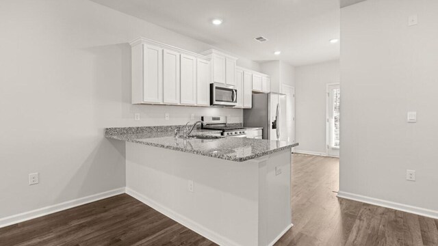 kitchen with kitchen peninsula, appliances with stainless steel finishes, dark hardwood / wood-style flooring, light stone counters, and white cabinets