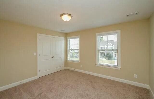 carpeted empty room featuring baseboards and visible vents