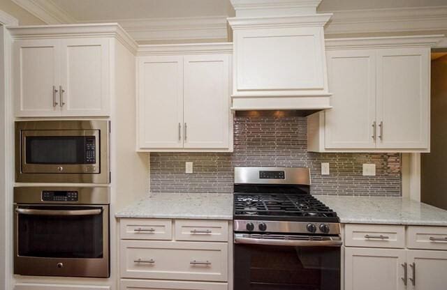 kitchen featuring white cabinets, stainless steel appliances, tasteful backsplash, and light stone countertops