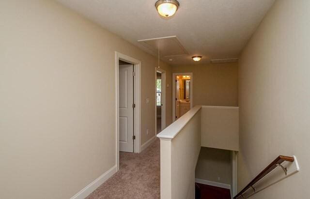 corridor featuring attic access, light carpet, an upstairs landing, and baseboards