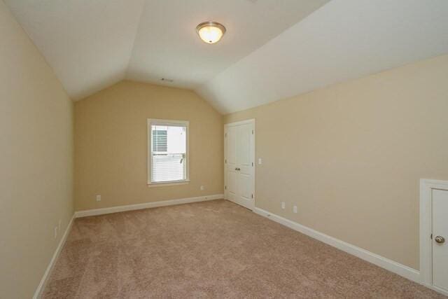 additional living space with vaulted ceiling, light carpet, and baseboards
