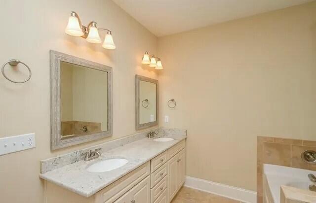 bathroom with a tub, double vanity, baseboards, and a sink