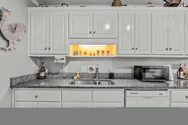 kitchen with white cabinetry, dark stone countertops, dishwasher, and sink