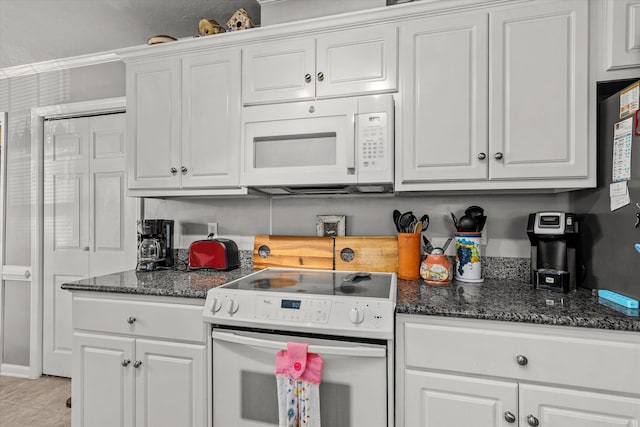 kitchen featuring dark stone countertops, white cabinetry, and stove