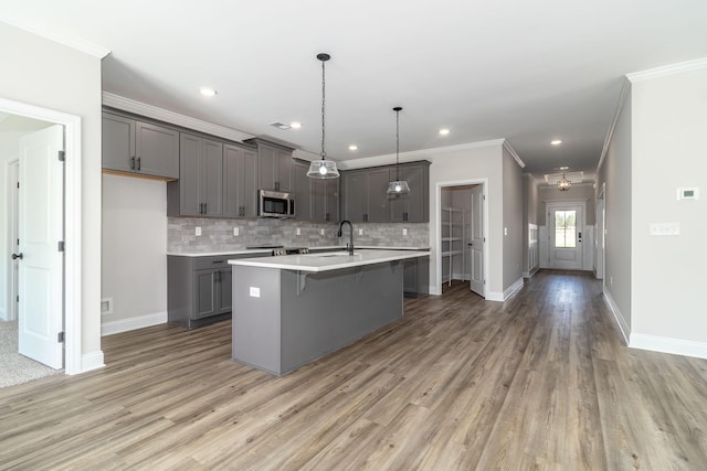 kitchen with hanging light fixtures, gray cabinets, light wood-type flooring, an island with sink, and a kitchen bar