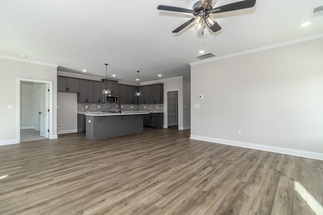 kitchen featuring decorative backsplash, dark hardwood / wood-style flooring, a kitchen island with sink, crown molding, and decorative light fixtures