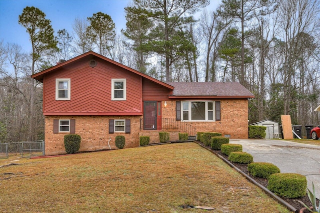 tri-level home featuring brick siding, a front lawn, an outdoor structure, and fence