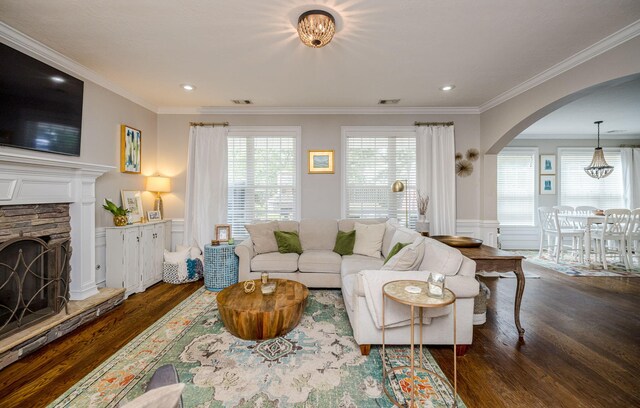 living room with a stone fireplace, crown molding, and dark wood-type flooring