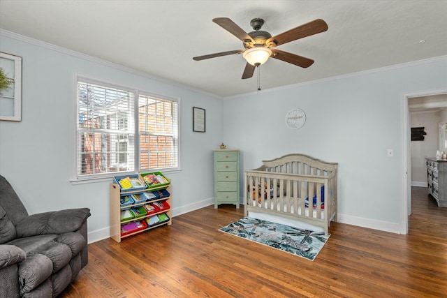 bedroom with ceiling fan, baseboards, ornamental molding, wood finished floors, and a nursery area