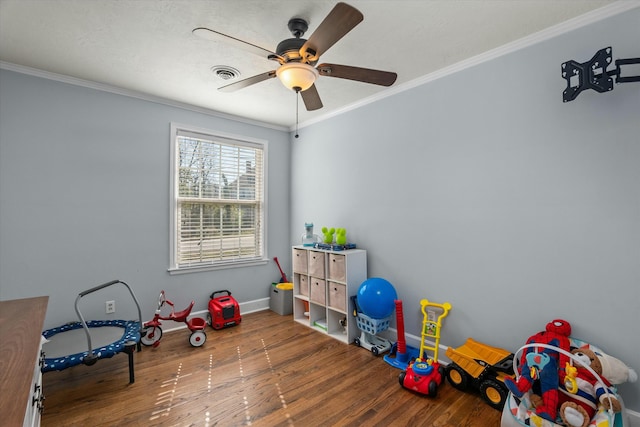 rec room featuring visible vents, baseboards, ornamental molding, wood finished floors, and a ceiling fan