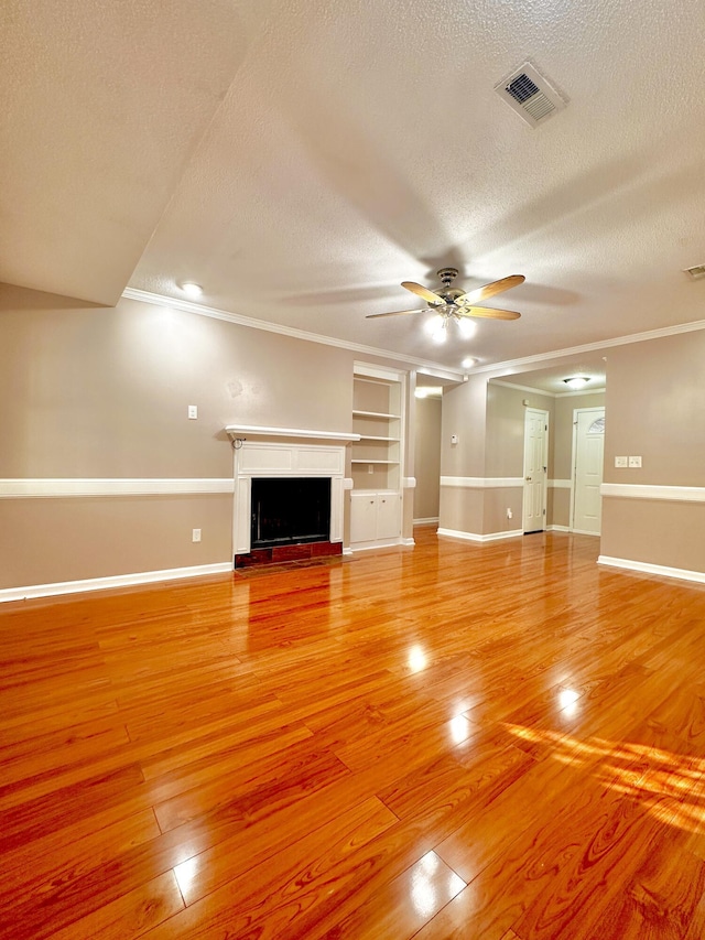 unfurnished living room with ceiling fan, light wood-type flooring, a textured ceiling, and ornamental molding