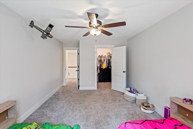 unfurnished bedroom featuring carpet, a spacious closet, baseboards, and a ceiling fan