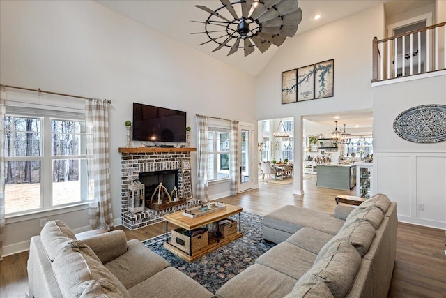 living area featuring a decorative wall, a brick fireplace, wood finished floors, high vaulted ceiling, and ceiling fan with notable chandelier