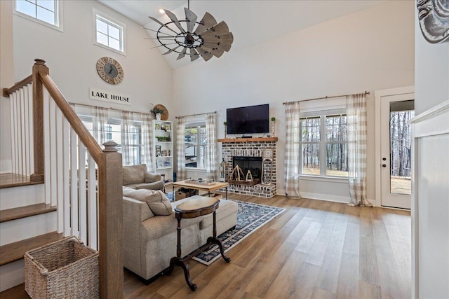 living area with a fireplace, a high ceiling, ceiling fan, wood finished floors, and stairs