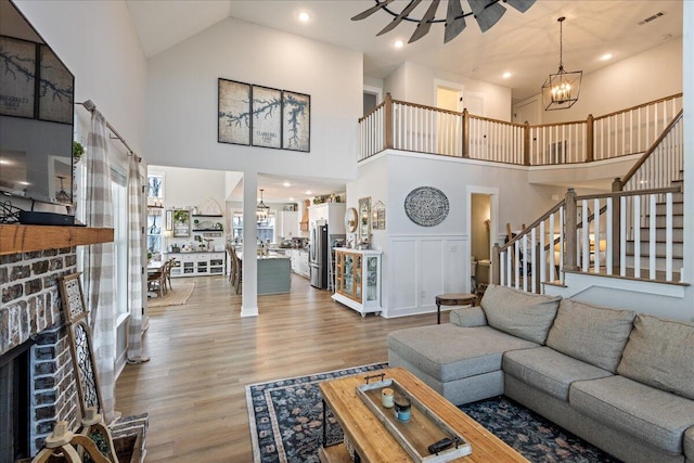 living area featuring ceiling fan with notable chandelier, a fireplace, visible vents, stairway, and light wood-type flooring