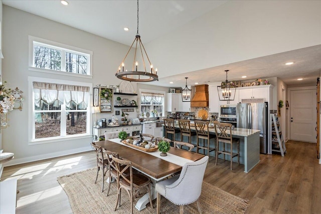 dining space with baseboards, wood finished floors, a high ceiling, a chandelier, and recessed lighting