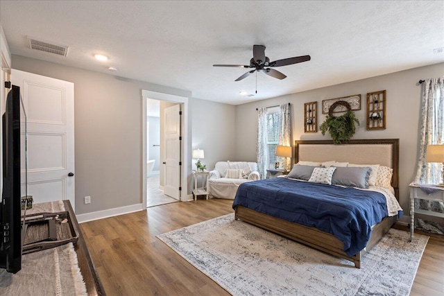 bedroom with ensuite bathroom, wood finished floors, a ceiling fan, visible vents, and baseboards