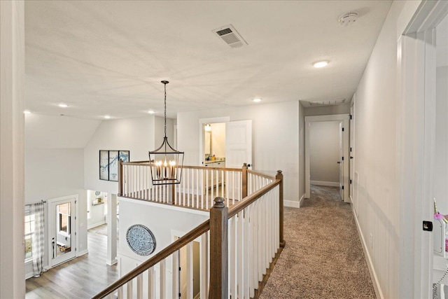 hallway featuring visible vents, light carpet, an upstairs landing, a chandelier, and baseboards