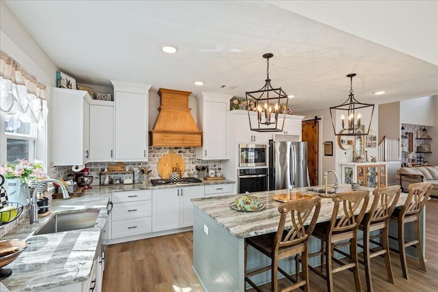 kitchen featuring light wood finished floors, custom exhaust hood, stainless steel appliances, backsplash, and a sink