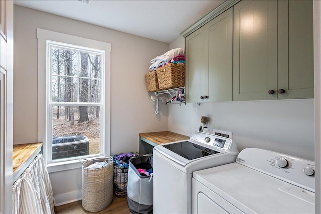 clothes washing area featuring wood finished floors, cabinet space, and washer and dryer