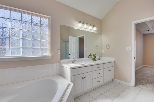 bathroom featuring tile patterned flooring, vanity, a relaxing tiled tub, and vaulted ceiling