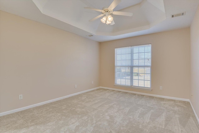 empty room with light carpet, a tray ceiling, and ceiling fan