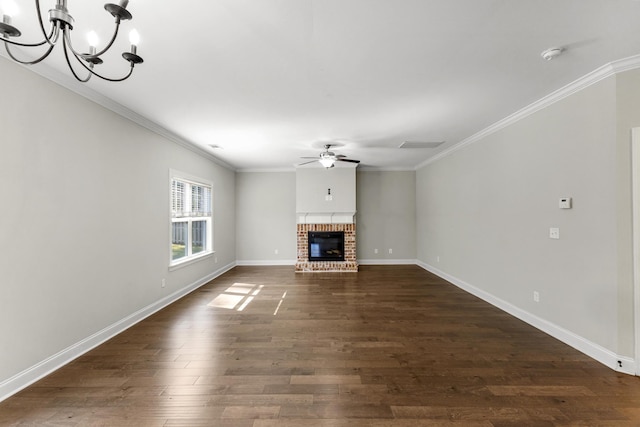 unfurnished living room featuring ornamental molding, ceiling fan with notable chandelier, a brick fireplace, and dark wood-type flooring