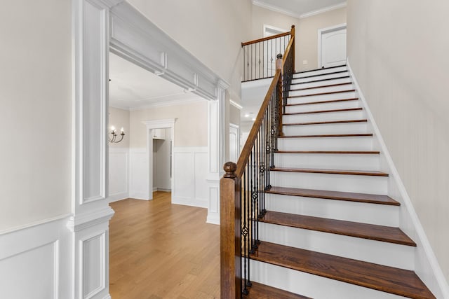 stairway with wood-type flooring, ornamental molding, and an inviting chandelier