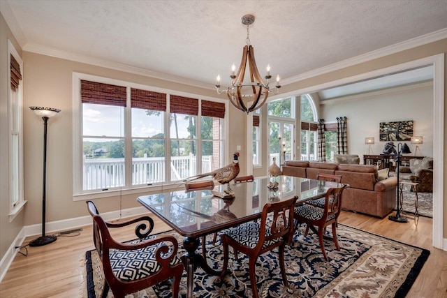 dining room with light wood-type flooring, ornamental molding, a wealth of natural light, and an inviting chandelier