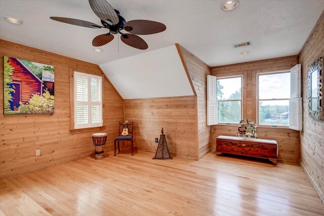 bonus room featuring light wood-type flooring, a textured ceiling, vaulted ceiling, ceiling fan, and wooden walls