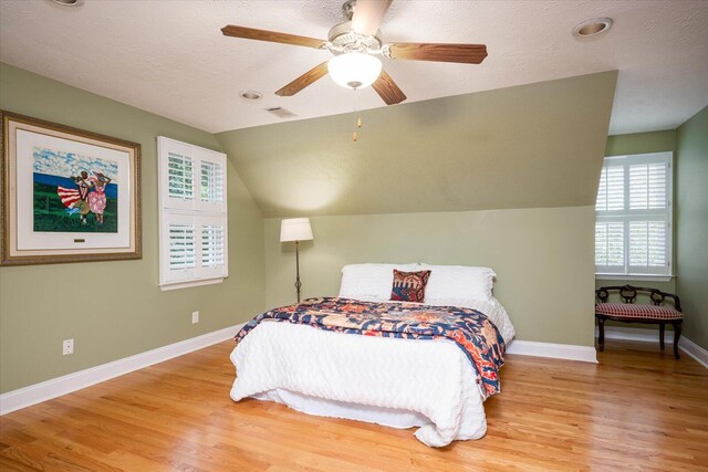 bedroom featuring ceiling fan, lofted ceiling, a textured ceiling, and light hardwood / wood-style flooring