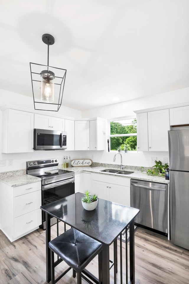 kitchen with sink, hanging light fixtures, stainless steel appliances, light hardwood / wood-style flooring, and white cabinets