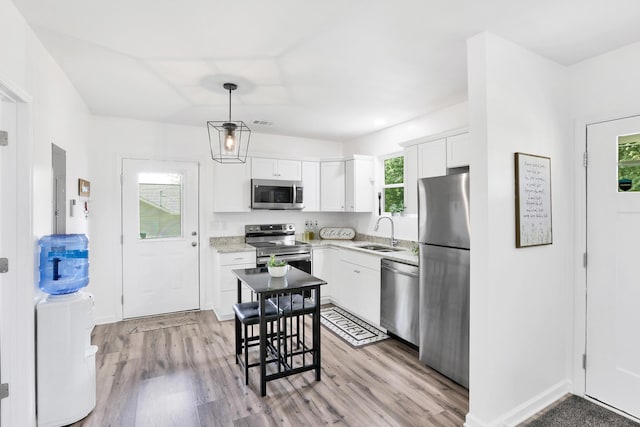 kitchen featuring white cabinetry, sink, stainless steel appliances, light hardwood / wood-style flooring, and decorative light fixtures