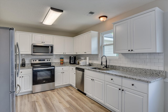 kitchen with visible vents, appliances with stainless steel finishes, tasteful backsplash, a sink, and light wood-style flooring