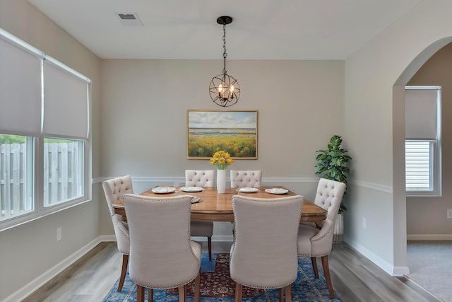 dining space featuring arched walkways, a healthy amount of sunlight, and wood finished floors
