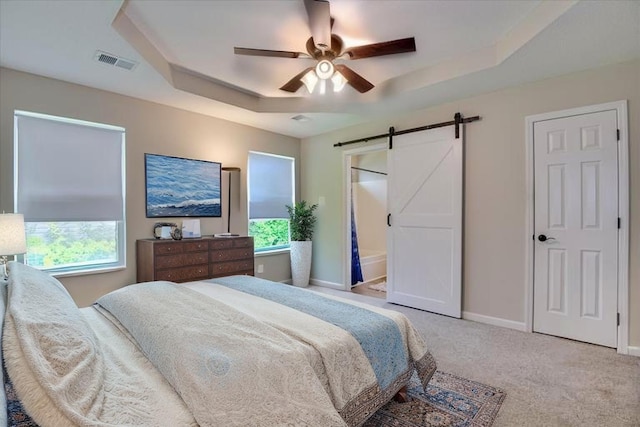 carpeted bedroom featuring a raised ceiling, multiple windows, a barn door, and visible vents